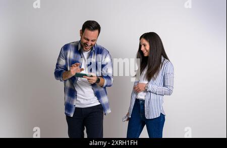Lächelnde junge Freundin, die einen Gamer-Freund ansieht, der Videospiele über das Smartphone spielt. Fröhliches Paar in Casuals gekleidet mit Handys stehend A Stockfoto