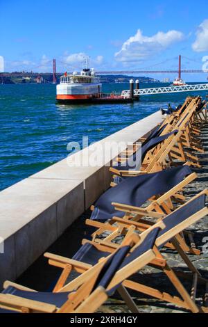 Lissabon, Portugal. Liegestühle am Fluss Tejo mit Blick auf die Brücke vom 25. April. März 2017 Stockfoto