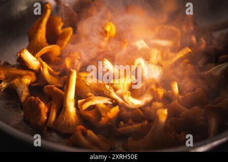 Pfifferlingen werden in einer Pfanne gebraten. Die goldene Farbe der Pilze wird durch Sonnenlicht durch den Rauch beleuchtet. Hochwertige Fotos Stockfoto