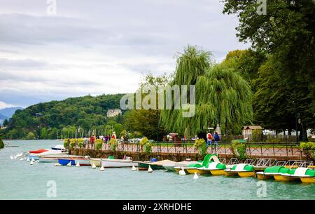 Die Seepromenade von Annecy (Haute-Savoie, Frankreich) am Abend. Nicht erkennbare Menschen auf der Promenade in der Nähe von Anlegestellen Wassertretbooten. Stockfoto