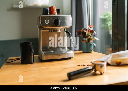 Eine gemütliche Küchenszene mit moderner Kaffeemaschine, Mahlwerk und einer Tasse auf einem Holztisch mit einer kleinen Pflanze und Fenster im Hintergrund Stockfoto
