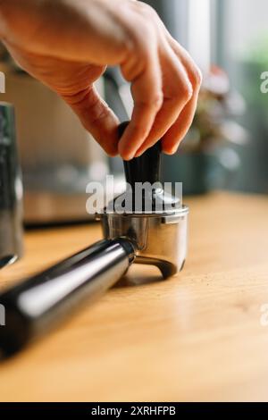 Nahaufnahme einer Hand, die Kaffeesatz in einem Portafilter auf einer Holzoberfläche stampft Stockfoto