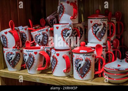 Colmar, Frankreich - 4. Juni 2023: Keramikbecher mit traditionellen elsässischen Motiven, Störche, Lebkuchenmann und Brezeln in einem Souvenirladen Stockfoto