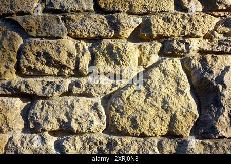 Detaillierte Textur einer verwitterten Steinmauer aus großen Felsbrocken unter natürlichem Licht. Stockfoto