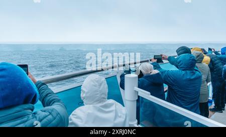 Antarktis - 26. Dezember 2023 - Foto des Eisbergs A23a vom Kreuzfahrtschiff hinter Menschenmenge. Passagiere halten Handys hoch, um es zu fotografieren Stockfoto