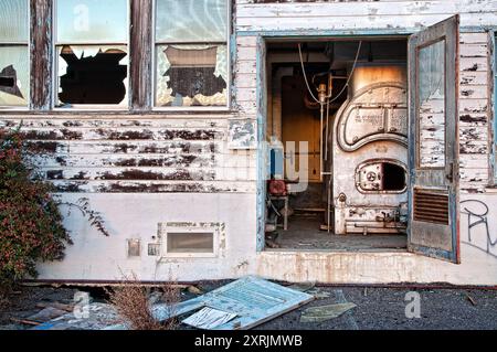 In einer verlassenen Werft bricht ein altes Gebäude auseinander. Kaputte Fenster und ein klassischer Industriekessel sind durch eine offene Tür sichtbar. Stockfoto