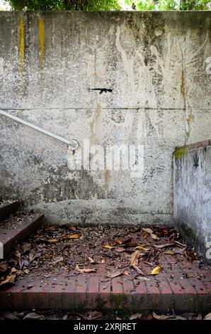 Die Stadtbesichtigung zeigt eine grobe Zeichnung auf einer grundierten Wand, die eine Schusswaffe im Militärstil wie eine AR-15 über einer mit Blättern übersäten Treppe darstellt. Stockfoto