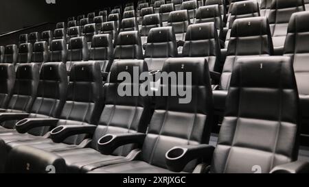 Reihen leerer Kinositze aus schwarzem Leder mit Getränkehalter und nummerierten Rückenlehnen in einem modernen Kino Stockfoto