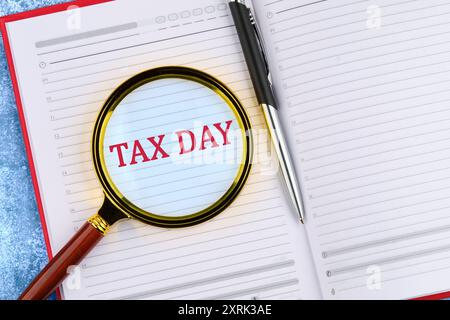 Tax Day Tax Financial Money Money Konzept. Worte STEUERN DEN TAG durch eine Lupe in einem offenen Business-Notizbuch. Stockfoto