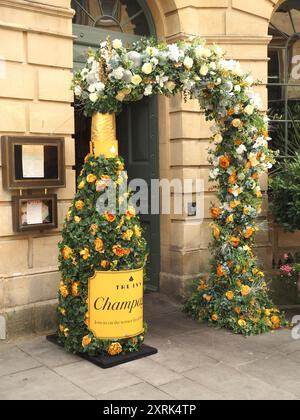 Blumenbogen und riesige verzierte Champagnerflasche vor der Tür zum Ivy, Milsom Street, Bath. Stockfoto