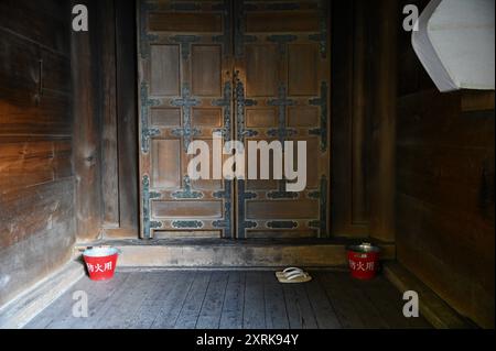 Traditioneller japanischer Hauseingang mit einer antiken Holztür, Geta-Sandalen und zwei rot verzinkten eisernen Feuerschutzeimern in Nara Kansai Japan. Stockfoto