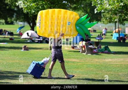 Uttenweiler, Deutschland. August 2024. Ein Mann kommt am Sonntagmorgen mit einer aufblasbaren Luftmatratze in Ananasform auf der Schulter in das Uttenweiler Freibad. Autor: Thomas Warnack/dpa/Alamy Live News Stockfoto