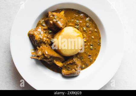 Blick von oben auf nigerianische Ogbono-Suppe und eba auf einem weißen Teller, Blick von oben auf Ogbono-Suppe mit garri und verschiedenen Fleischsorten auf einem Suppenteller Stockfoto