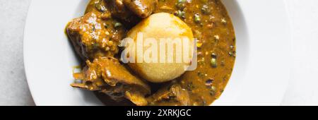 Blick von oben auf nigerianische Ogbono-Suppe und eba auf einem weißen Teller, Blick von oben auf Ogbono-Suppe mit garri und verschiedenen Fleischsorten auf einem Suppenteller Stockfoto