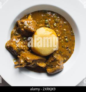 Blick von oben auf nigerianische Ogbono-Suppe und eba auf einem weißen Teller, Blick von oben auf Ogbono-Suppe mit garri und verschiedenen Fleischsorten auf einem Suppenteller Stockfoto