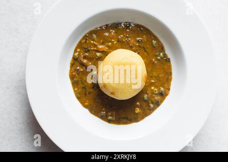 Blick von oben auf nigerianische Ogbono-Suppe und eba auf einem weißen Teller, Blick von oben auf Ogbono-Suppe mit garri und verschiedenen Fleischsorten auf einem Suppenteller Stockfoto