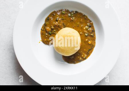 Blick von oben auf nigerianische Ogbono-Suppe und eba auf einem weißen Teller, Blick von oben auf Ogbono-Suppe mit garri und verschiedenen Fleischsorten auf einem Suppenteller Stockfoto