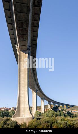 Stahlbetonbrücke von unten gesehen, kurvenförmig und mit blauem Himmel im Hintergrund, in Portugal. Stockfoto