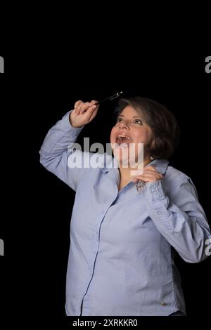 Eine Frau hält eine Brille und lacht. Sie trägt ein blaues Hemd und hat ein Lächeln im Gesicht Stockfoto