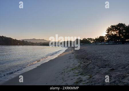 Die atemberaubende Schönheit der Playa de la Ladeira in Baiona bei Sonnenaufgang. Wenn die Sonne aufgeht, taucht ihr goldenes Licht den Sandstrand und das ruhige Wasser und schafft so Stockfoto