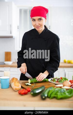 Positive weibliche Küchenchefin in schwarzer Uniform, die Gemüsegericht zubereitet Stockfoto