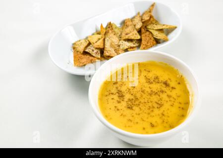 Kürbiscremesuppe in weißer Schüssel mit dünnen Brotchips auf weißem Tisch Stockfoto