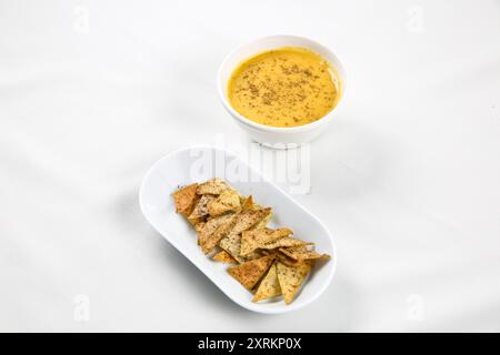 Kürbiscremesuppe in weißer Schüssel mit dünnen Brotchips auf weißem Tisch Stockfoto