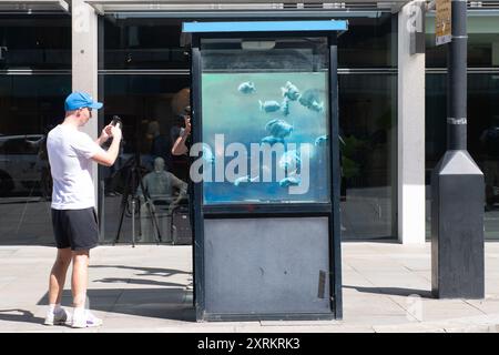 London, Großbritannien. August 2024. Die Leute machen Fotos von einem siebten neuen Wandbild des Street Artist Banksy, das Piranha-Fische auf einer Polizeiwache in Ludgate Hill, City of London, zeigt. Quelle: Justin Ng/Alamy Live News Stockfoto