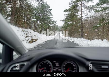 Winterstraße durch die bewaldete Gegend aus dem Inneren des Autos Stockfoto