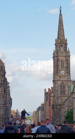 Mann auf Stelzen inmitten der Menschenmassen auf der Royal Mile mit Kirche direkt während des Fringe Festivals in Edinburgh Schottland. August 2024 Stockfoto