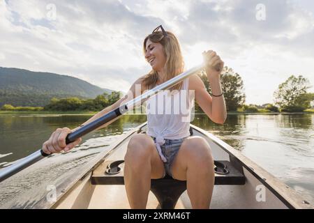 Lächelnde Frau, die ein Kanu paddelt, entspannt und genießt die natürliche Umgebung und den sonnigen Tag, Vorderansicht. Kanu- und Freizeitkonzept. Stockfoto