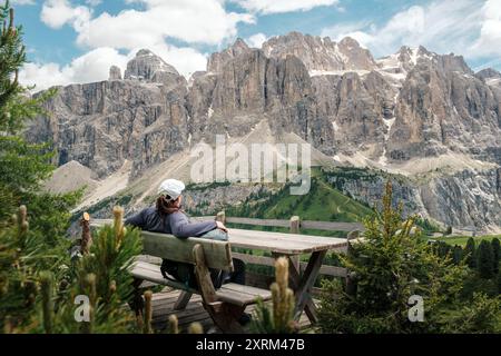 Eine Frau entspannt sich auf einer Bank und blickt über den Gardenapass auf die großen Dolomiten der Sellagruppe im Sommer in Italien. Stockfoto