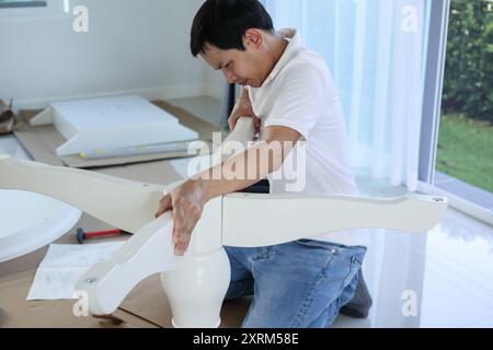 Asiatischer Mann, der weiße Tischmöbel zu Hause zusammenbaut Stockfoto