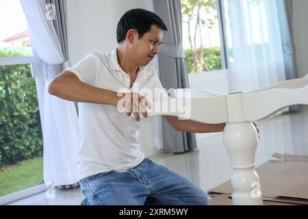 Asiatischer Mann, der weiße Tischmöbel zu Hause zusammenbaut Stockfoto