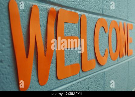 Ein Willkommensschild aus orangefarbenem Bastelpapier an einer Wand aus Schlackenblöcken in einem Klassenzimmer. Stockfoto