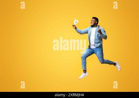 Euphorisch afro Mann springen mit Bargeld in der Hand auf gelbem Hintergrund Stockfoto