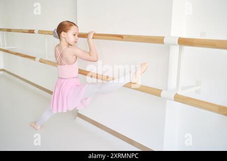 Ein junges Ballettmädchen beim Studiounterricht. Trainingsleistung. Stretching-Übungshaltung. Ballerina-Praxis-Balance-Technik. Klassische Eleganz Fitness. Tanzkostüm, Garn. Pinkfarbenes Kleid, Rock Stockfoto