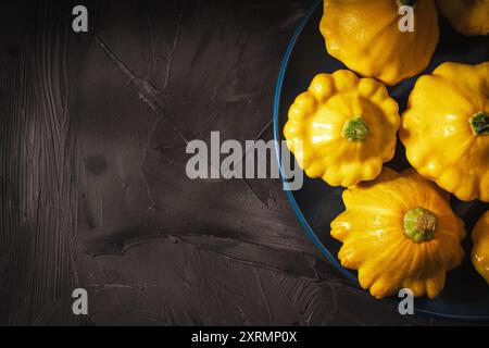 Kleine gelbe Kürbisse auf blauem Teller auf schwarzem, strukturiertem Hintergrund. Ein Ort zum Kopieren des Bereichs. Für Bannerlayout verwenden. Hochwertige Fotos Stockfoto