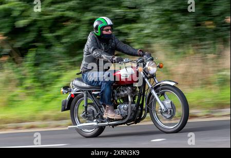 Potterspury, Northants, Großbritannien - 11. August 2024: Mann mit einem roten Triumph Bonneville-Motorrad aus dem Jahr 1973 auf einer britischen Straße Stockfoto