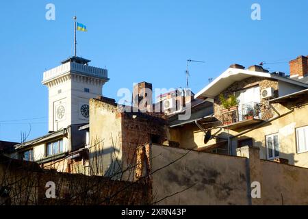 Die Flagge der Ukraine fliegt stolz auf dem Rathaus in Lemberg und überblickt charmante alte Gebäude unter einem klaren blauen Himmel. Stockfoto