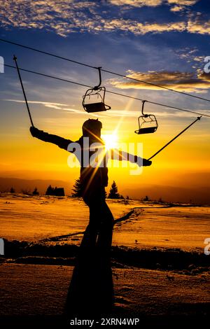 Silhouette eines Skifahrers, der bei Sonnenuntergang Stöcke hält, mit einer beeindruckenden Winterlandschaft und Skilift im Hintergrund. Wunderschöne Farben und Atmosphäre. Stockfoto