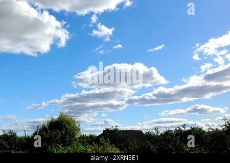 Flauschige weiße Wolken schweben über einem hellblauen Himmel und werfen Schatten über das üppige Grün der friedlichen Landschaft. Stockfoto