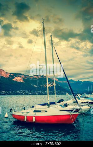 Yachten legen bei Sonnenuntergang am Annecy Lake an. Annecy Lake ist eines der beliebtesten französischen Resorts. Retro-Foto im Alter. Stockfoto