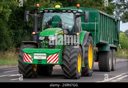 Potterspury, Northants, Großbritannien - 11. August 2024: Grüner John Deere 6r-Traktor zieht einen Anhänger auf einer britischen Landstraße Stockfoto