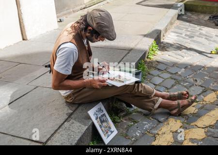 Edinburgh, Schottland, Großbritannien. August 2024. Ein Künstler, der während des Edinburgh Fringe Festivals auf dem Bürgersteig sitzt. Quelle: Skully/Alamy Live News Stockfoto