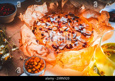 Hausgemachter Apfelkuchen mit Preiselbeeren auf dem Tisch mit gebrühtem Kräutertee, Sanddorn und Kamillenblüten auf einer Leinenserviette. Hohe Qual Stockfoto