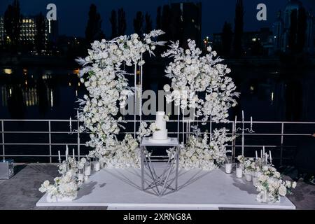 Hochzeitseinrichtung mit dreistufigem weißem Kuchen mit Blumenakzenten. Hochzeitsinspiriert, luxuriöse Veranstaltungen Stockfoto