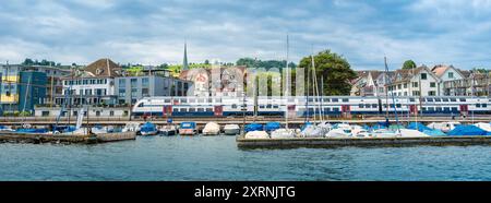 Wadenschwil, Schweiz - 1. Juli 2024: Ein Zug der Schweizerischen Bahn fährt am Zürcher See am Jachthafen in Wadenswil vorbei Stockfoto