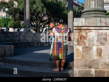 Eine guatemaltekische Frau in bunten traditionellen Kleidern und ihr Sohn im Parque Centro América. Quetzaltenango, Guatemala. Stockfoto