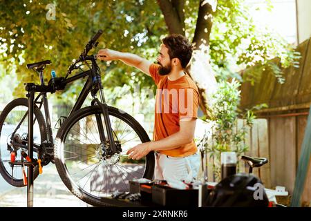 Jährliche Sommerfahrradwartung durch athletischen kaukasier für Outdoor-Freizeitradeln. Aktiver und gesunder männlicher Radfahrer, der das Fahrrad im Hof gründlich inspiziert und repariert. Stockfoto